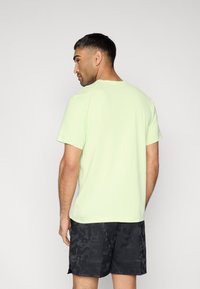 Ανοιχτό πράσινο κοντομάνικο μπλουζάκι από απαλό ύφασμα, με στρογγυλή λαιμόκοψη, σε συνδυασμό με σκούρα σορτς σε παραλλαγή, από πίσω όψη.