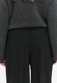 Ciemnozielone spodnie w dopasowanym kroju, z kieszeniami bocznymi i gładką teksturą, połączone z szarym swetrem z dzianiny.