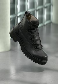Stivaletto alla caviglia in pelle nera con chiusura stringata, finitura testurizzata, punta rotonda, suola robusta e linguetta posteriore.