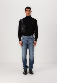 Pulover negru body-fit cu gât, blugi denim albaștri și pantofi din piele negri. Asortat cu o geantă crossbody neagră, cu logo-uri albe.
