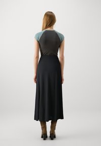 Jupe noire avec un design long et fluide et un haut ajusté à manches courtes en teal et gris foncé. Des bottes brunes jusqu'aux genoux complètent le look.