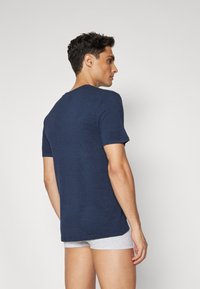 T-shirt de manga curta azul marinho com textura canelada e gola redonda. Modelo a usar boxers cinzentos, visto de costas.