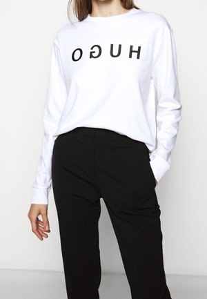 Vit långärmad sweatshirt med svart tryckt text, i kombination med svarta skräddarsydda byxor. Slät tyg och avslappnad passform.