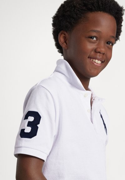 Balta polo krekls ar īsām piedurknēm, kreisajā rokā zilgani tumšs skaitlis 3 un krāsains logotips uz krūtīm. Mīksta tekstūra, apkakles dizains.