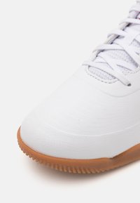 Weißer Sneaker mit einem glatten, strukturierten Obermaterial aus Synthetik, einer hellgrauen Mesh-Zunge und einer Gummisohle mit einem geriffelten Muster.