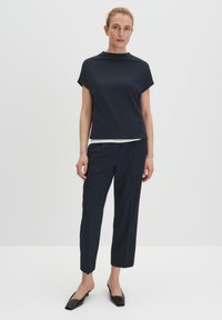 Marineblauwe top met een hoge halslijn en korte mouwen, gecombineerd met bijpassende taps toelopende broek en zwarte puntige ballerina's. Soepele stoftextuur.