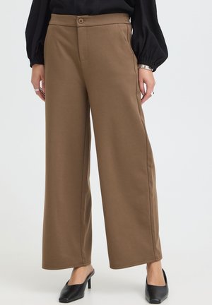Pantalon marron à jambes larges avec bouton devant et poches, porté avec des chaussures à talons noires et un haut noir à manches longues.