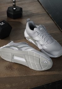 Paire de chaussures de sport Adidas grises sur un sol en bois à côté de deux haltères hexagonaux noirs de 25 livres.