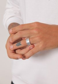 Silberner, hammerstrukturierter Ring, der an einem Finger getragen wird, mit sichtbaren Hauttönen und einem kleinen Tattoo. Die Hände sind in entspannter Position dargestellt.