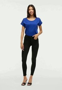 Modra kratka majica s kratkimi rokavi, združena s črnimi oprijetimi hlačami, ki imajo gladko teksturo in prilega zasnovo, dopolnjena s črnimi petkami.