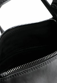 Interior de una bolsa de cuero negro con superficie texturizada, cierre de cremallera y herrajes en tono plateado. El interior es suave y está forrado.