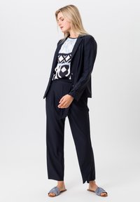 Marineblazer over een geblokt shirt met lichtblauwe en zwarte ontwerpen, gecombineerd met marineblauwe broek en blauwe crossover sliders.