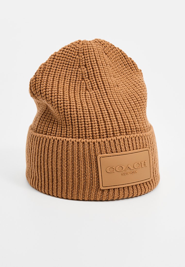 Brun stickad mössa med vikbar uppvik och en rektangulär läderlapp präglad med "COACH New York"-logotypen.