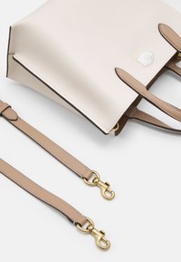 Torebka typu tote wykonana z teksturowanej kremowej skóry, z brązowymi akcentami, podwójnymi uchwytami oraz odpinanym beżowym paskiem na ramię z złotymi elementami.