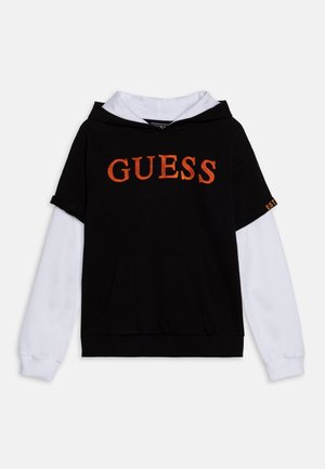 Czarna bluza z krótkim rękawem z kapturem nałożona na białą koszulę z długim rękawem, z napisem "GUESS" w kolorze pomarańczowym na przodzie.