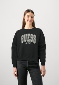 Felpa nera con la scritta "GUESS" e "Est. 1981" stampate in grigio. Presenta polsini e orlo a coste, vestibilità comoda e materiale in cotone morbido.