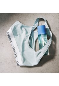 Soutien-gorge de sport bleu clair avec une ceinture blanche arborant le logo "Calvin Klein". Accompagné d'une bouteille bleue de CK Silky Coconut.