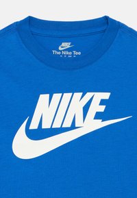 Modra bombažna majica s kratkimi rokavi z velikim belim logotipom "NIKE" in obliko požiranja. Okrogla ovratnik s ojačanim šivom. Oznaka znotraj ovratnika.