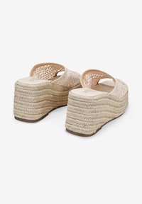 Sandalias cuña en beige con parte superior trenzada y plataforma de estilo espartano texturizada. Punta abierta redondeada y diseño sin talón. Suela plana de goma.