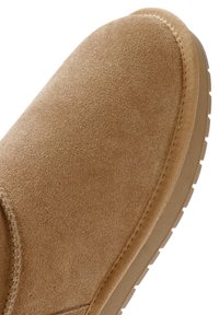 Scarpa in suede marrone con punta tonda, superficie testurizzata e suola in gomma. Presenta dettagli cuciti lungo il bordo.