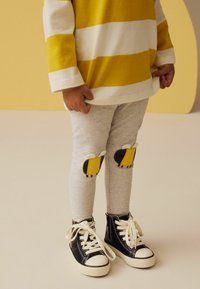Grau Leggings mit gelben und schwarzen Bienchen-Patch-Details an den Knien, kombiniert mit schwarzen High-Top-Sneakern und einem langärmligen, gestreiften Oberteil in Gelb.