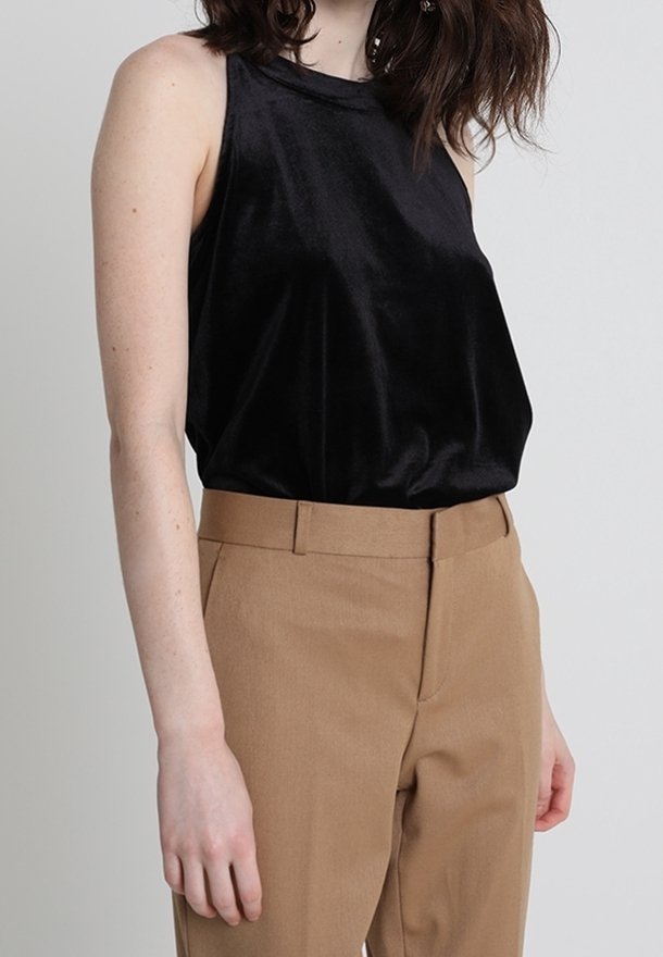 Femme portant un haut en satin noir sans manches rentré dans un pantalon taille haute couleur camel sur un fond uni.