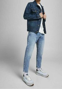 Jeansjacka i mörkblått med guldknappar, matchad med ljusblå jeans. Vita sneakers med grå och svarta detaljer fulländar outfiten.