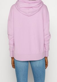 Pink hooded sweatshirt with a relaxed fit, ribbed cuffs and hem, and a smooth texture. Worn with blue jeans, shown from the back.