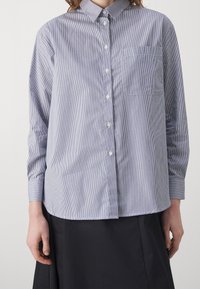 Camicia a maniche lunghe a righe blu e bianche con chiusura a bottoni, colletto aperto e taschino sul petto. Tessuto di cotone morbido con vestibilità comoda.