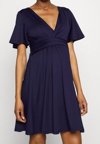 Mörkblå klänning i mjukt, stretchy tyg. Har en djup V-ringning, korta utsvängda ärmar och en empiremidja med samlade detaljer.