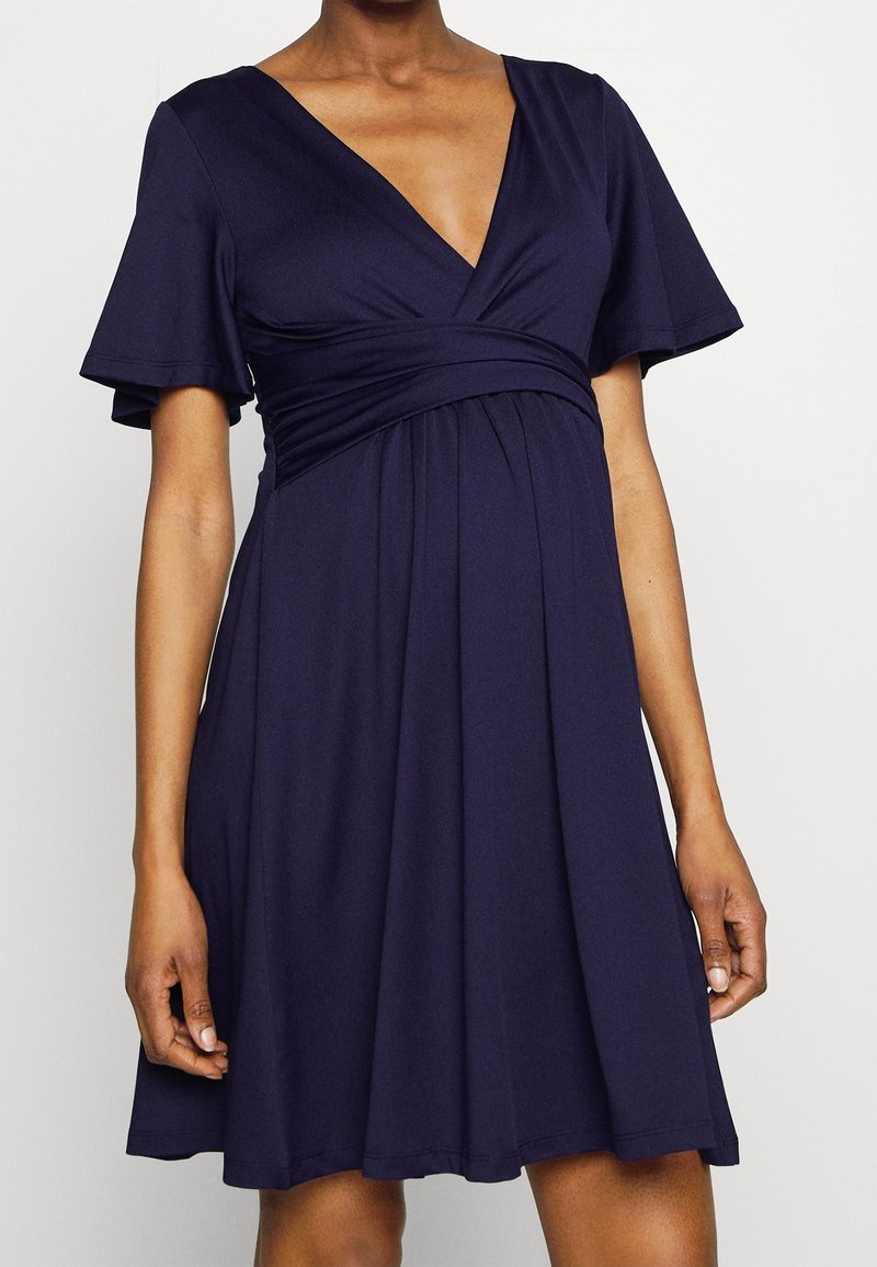 Mörkblå klänning i mjukt, stretchy tyg. Har en djup V-ringning, korta utsvängda ärmar och en empiremidja med samlade detaljer.