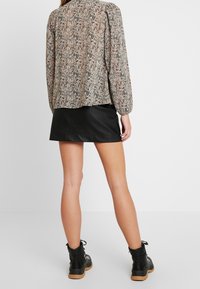 Blusa a maniche lunghe con motivo in beige, nero e rosa, dal taglio rilassato. Abbinata a una mini gonna di pelle nera e stivali ankle neri.