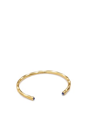 Brazalete abierto de oro con textura ligeramente martillada y pequeños detalles de piedra azul en cada extremo sobre un fondo blanco.