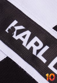 Tessuto a trama bianco e nero con la parola "KARL" in evidenza, insieme a un'etichetta rossa e arancione "10 ANNI" nell'angolo in basso.