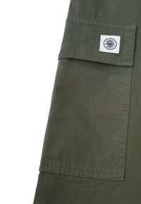 Olivengrüner Stoffbeutel mit einem weißen Etikett, das ein rundes Logo mit der Aufschrift "Ehrliche Regeln" zeigt, wobei eine glatte Textur und klare Linien zur Geltung kommen.