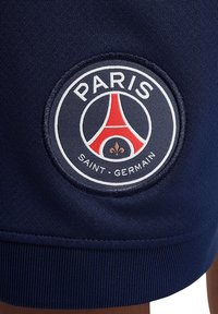 Pantaloni sportivi blu navy con un patch circolare in tessuto con il logo "Paris Saint-Germain", che include una Torre Eiffel stilizzata e un giglio.