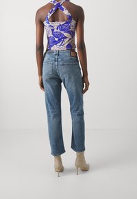 Blå denimjeans med rak skärning, uppvisade med en mönstrad lila och beige halterneck-topp. Skor med ljusa högklackade stövlar.