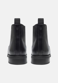Bottines noires en cuir avec panneaux latéraux élastiques, finition lisse et semelle noire robuste et texturée. Présente un minimum de couture et un détail logo.