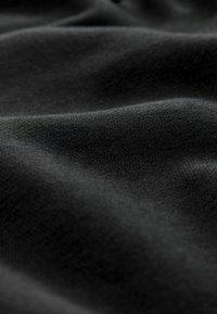 Schwarzer Stoff, der eine feine Textur und Weichheit zeigt, mit subtilen Wellen und Falten, die ein glattes Erscheinungsbild erzeugen.