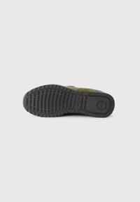 Black rubber outsole with deep tread, featuring green textile accents. Durable and textured design for enhanced grip and stability.