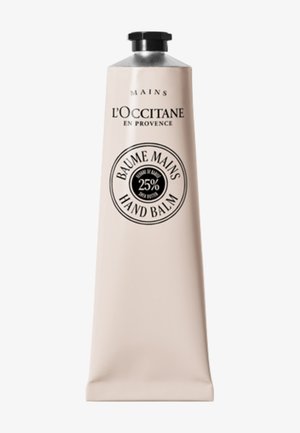 Baume pour les mains L'Occitane dans un tube rose pâle avec un bouchon argenté. Présente une étiquette circulaire noire indiquant "25% beurre de karité" et "Baume Mains".