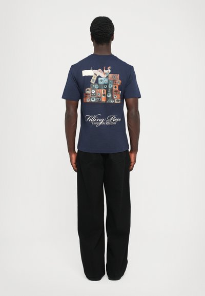 Himmelblaues Kurzarm-T-Shirt mit einem Grafikdesign von gestapelten Lautsprechern auf der Rückseite, kontrastierenden Elementen und dem Text "Filling Piece".
