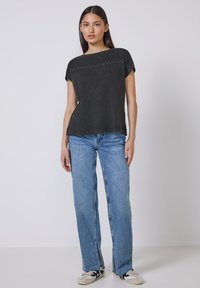 Sort kortærmet top med rund halsudskæring og nittedetaljer på brystet, parret med lyseblå lige ben-jeans og sneakers.