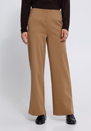 Person wearing high-waist wide-leg camel-colored pants with black loafers and a long-sleeve black top, standing on a plain background.