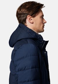 Granatowa kurtka puchowa z odpinanym kapturem, poziomym haftem, bocznym suwakiem oraz akcentami na zatrzask. Płaski krój kołnierza.