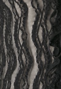 Svart spets tyg med vågiga texturerade mönster, som ligger ovanpå en beige bakgrund, med intrikata detaljer och en lätt, luftig känsla.