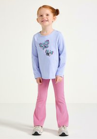 Lyseblå skjorte med lange ærmer og paliet sommerfugledesign, kombineret med lyserøde, strukturerede flared bukser og hvide sneakers.