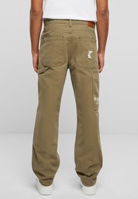 Pantalon cargo beige à coupe décontractée, avec plusieurs poches et un détail de marque brodé à l'arrière, fabriqué en matériau en coton durable.