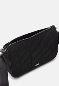 Quiltad svart nylon crossbody-väska med silverdetaljer, dragkedjestängning och justerbar rem; har DKNY-logotypen på framsidan.
