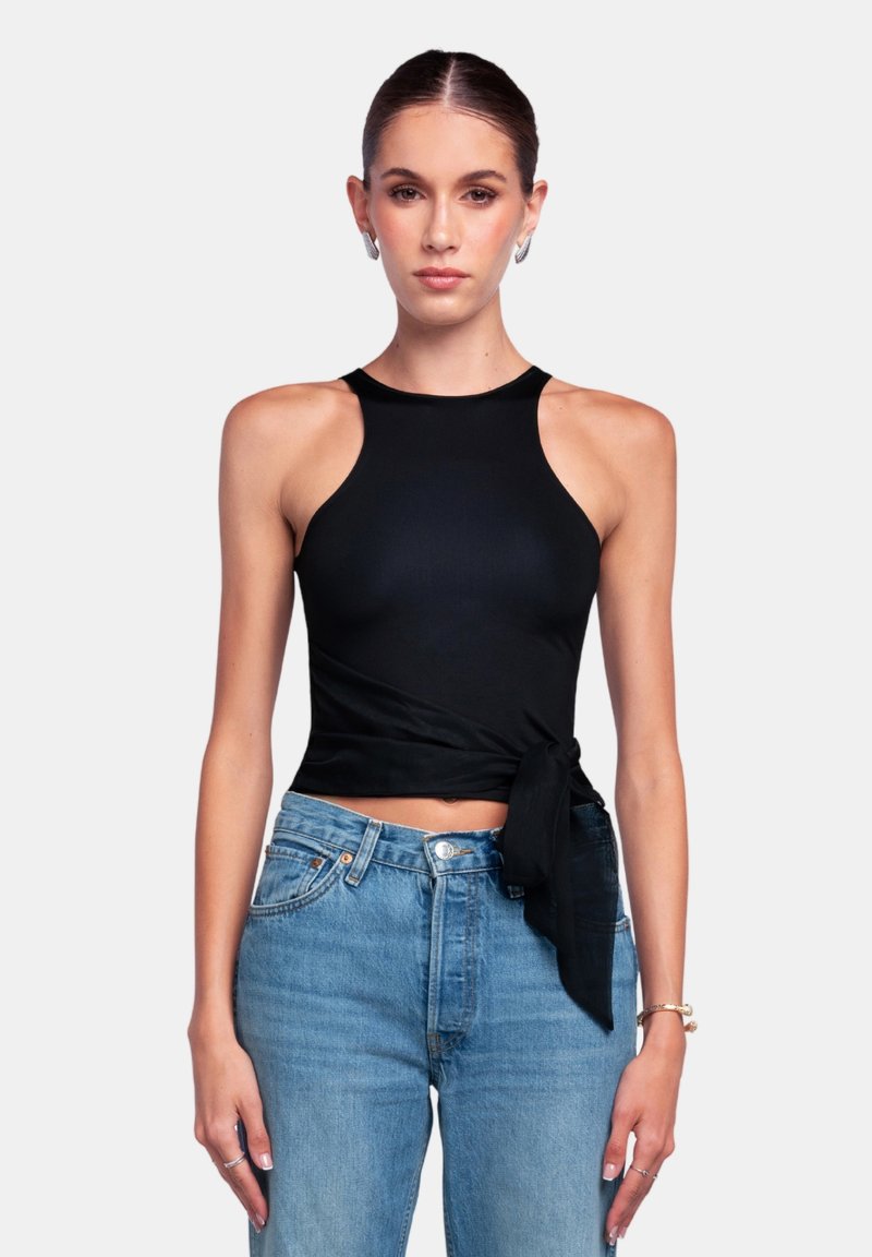 Top corto negro con un diseño sin mangas, cuello alto y un diseño envolvente que presenta un acento atado. Combinado con jeans de tiro alto en azul claro.